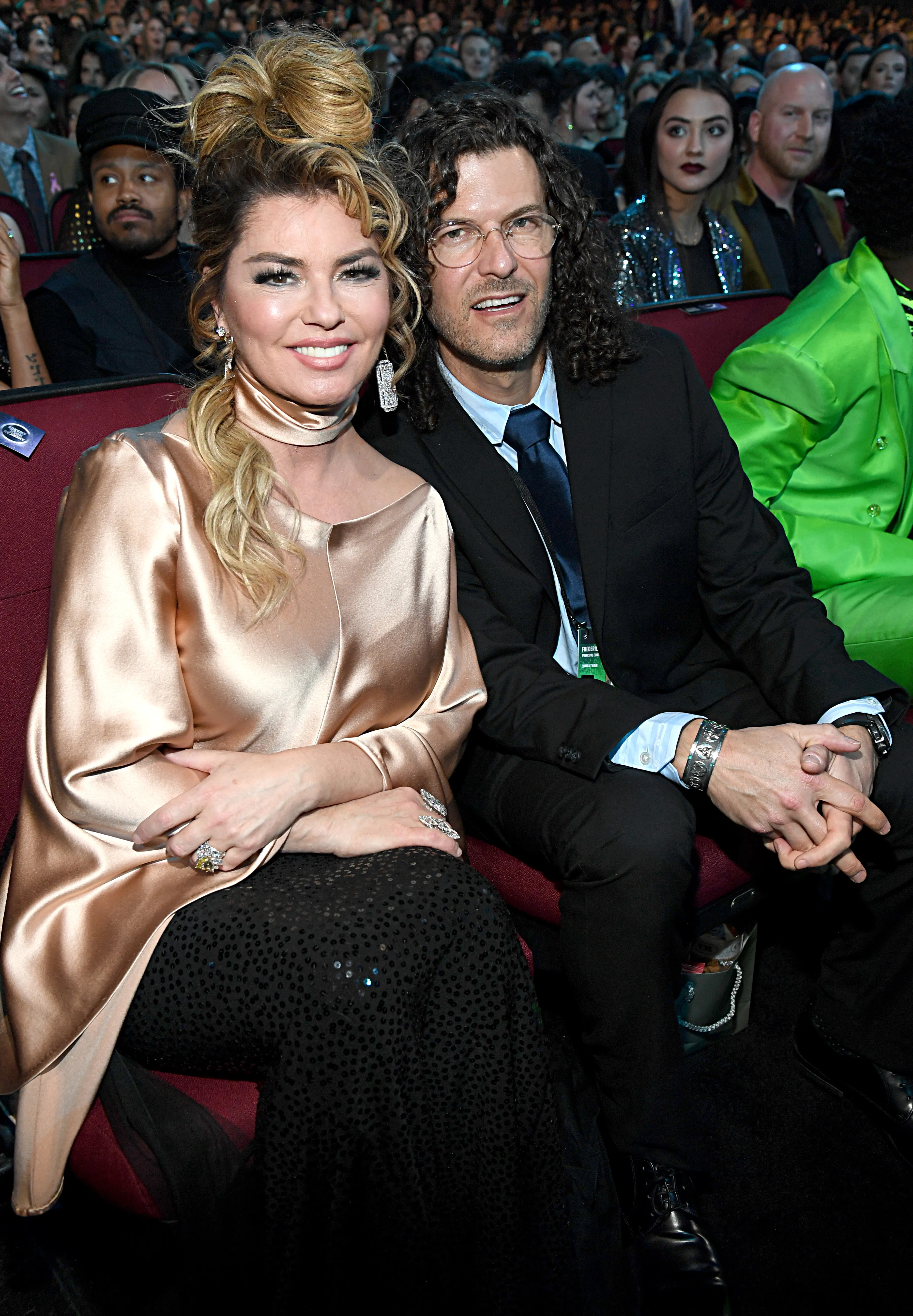 Shania Twain in a gold top and Frédéric Thiébaud in a suit sitting together at an awards show.