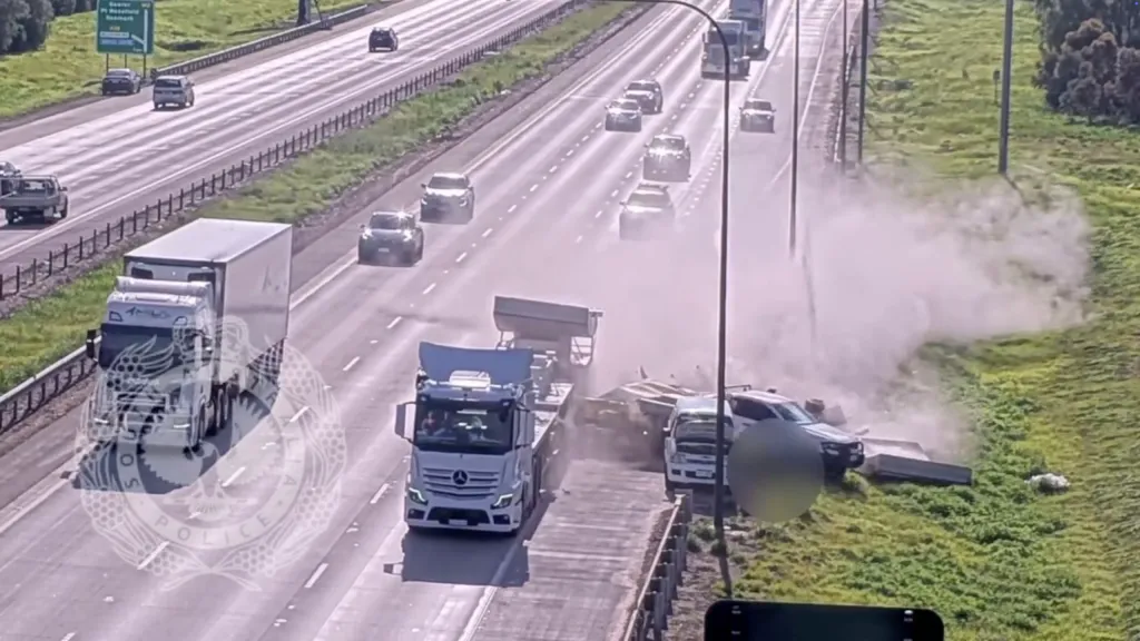 Dust erupts as concrete slabs fall from a truck and hit parked cars on the side of a highway.