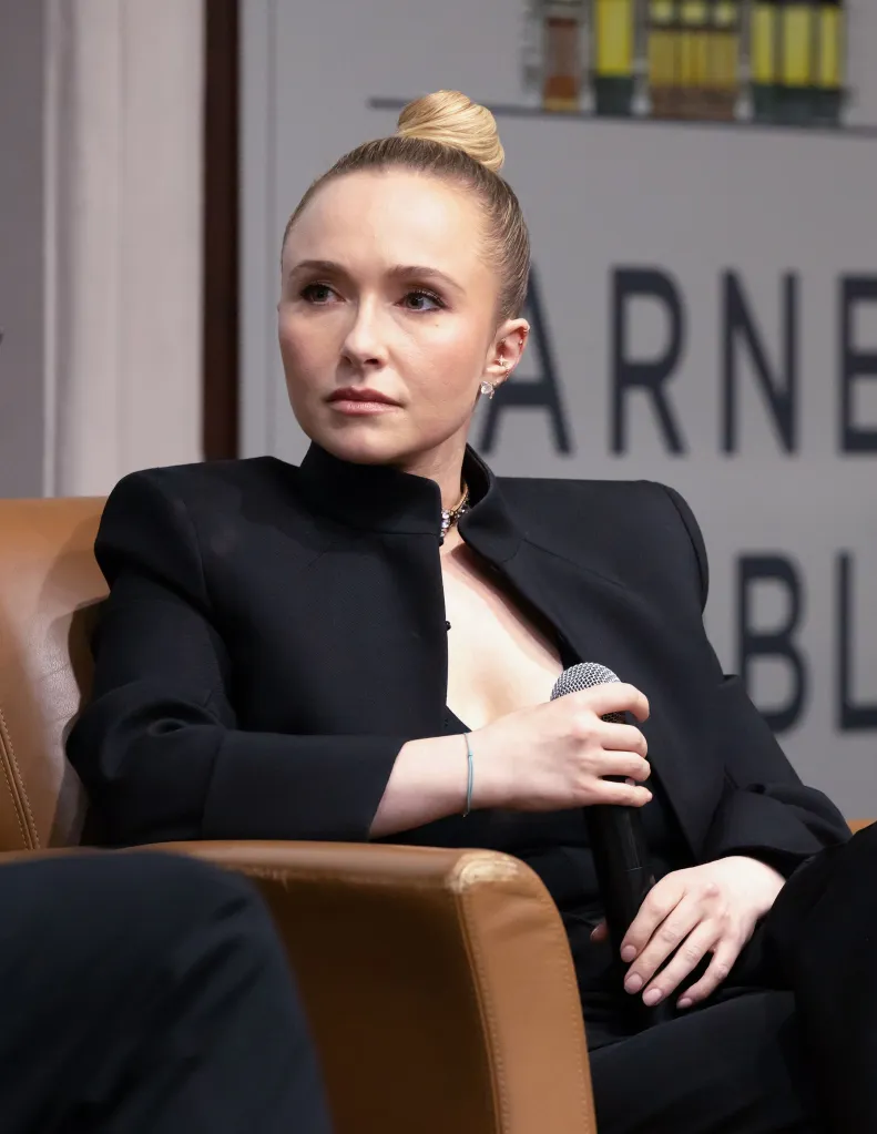Hayden Panettiere in a black top with her hair in a bun, holding a microphone, celebrating her new memoir.