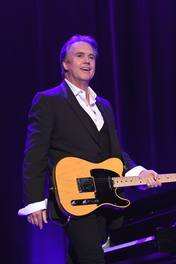 Shaun Cassidy performing on stage, holding a guitar.