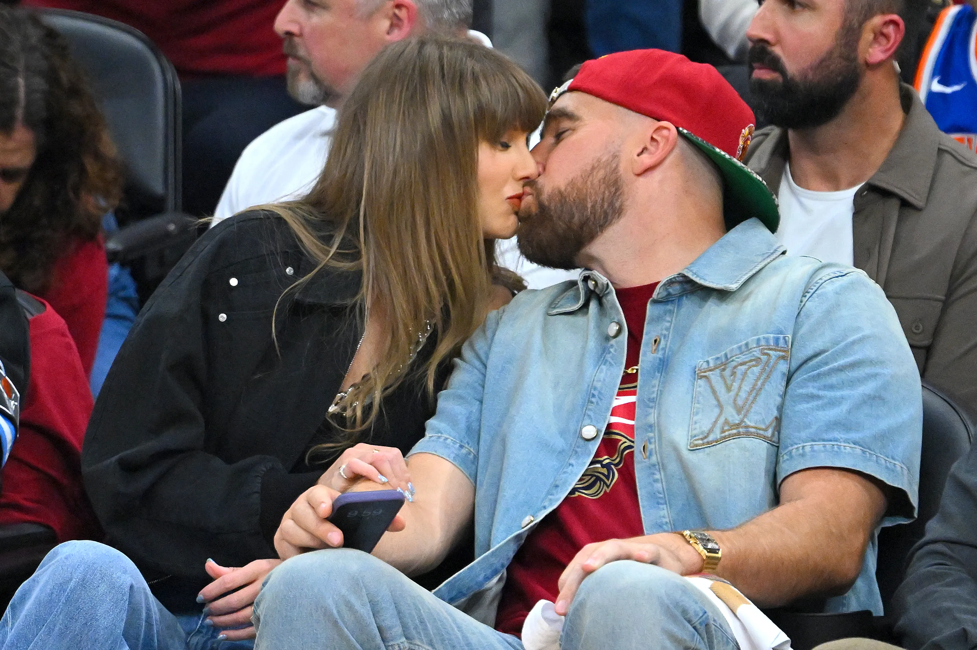 Singer Taylor Swift and Travis Kelce kissing during a basketball game.