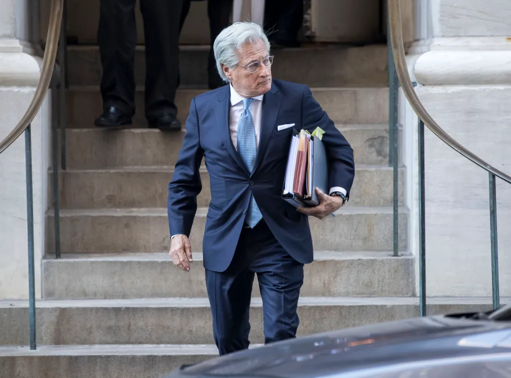 Marc Kasowitz, wearing a blue suit and tie, carries files while walking down stone steps outside the New York Supreme Court Appellate Division.