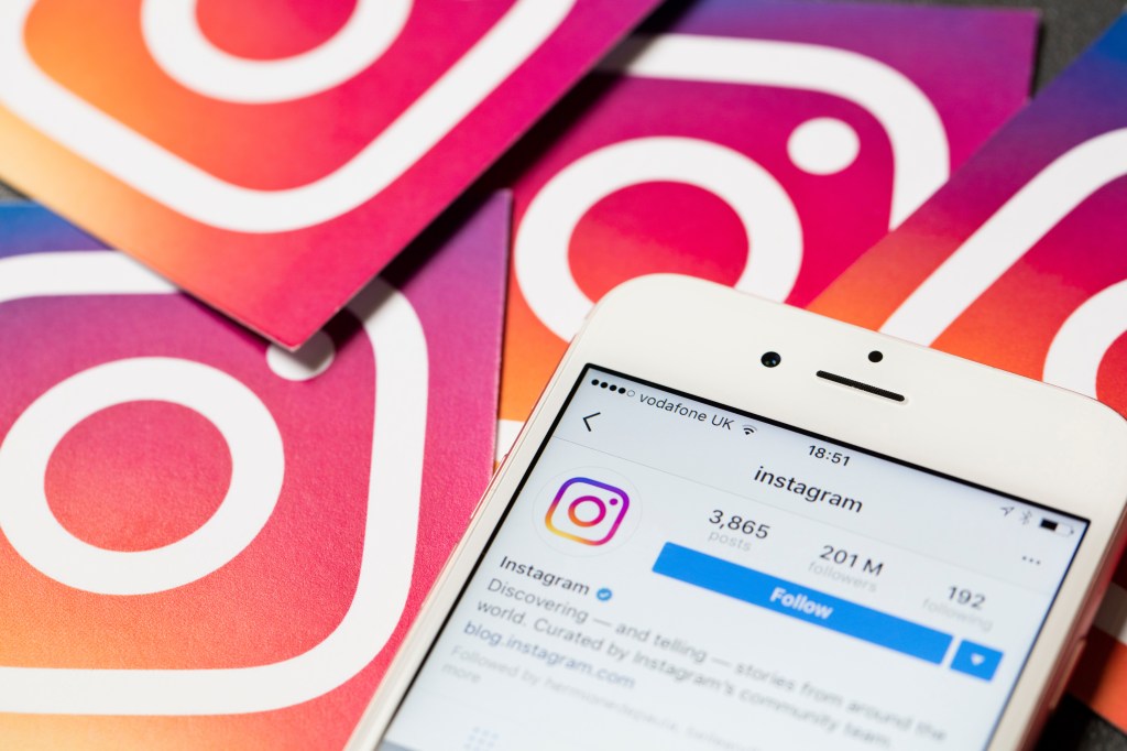A white iPhone displaying the Instagram app with other Instagram logos in the background.