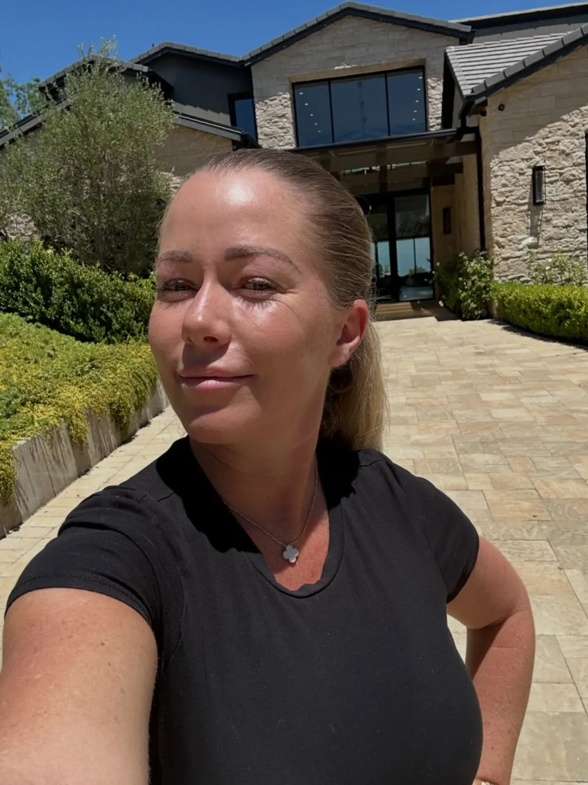 Kendra Wilkinson smiling at the camera in front of a large house.