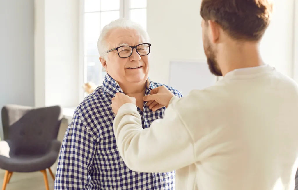 Adult son helping his senior father button his shirt.