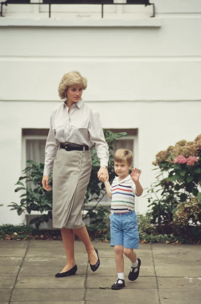 Diana, Princess of Wales, holding hands with her son Prince William, who is waving, walking on a sidewalk.