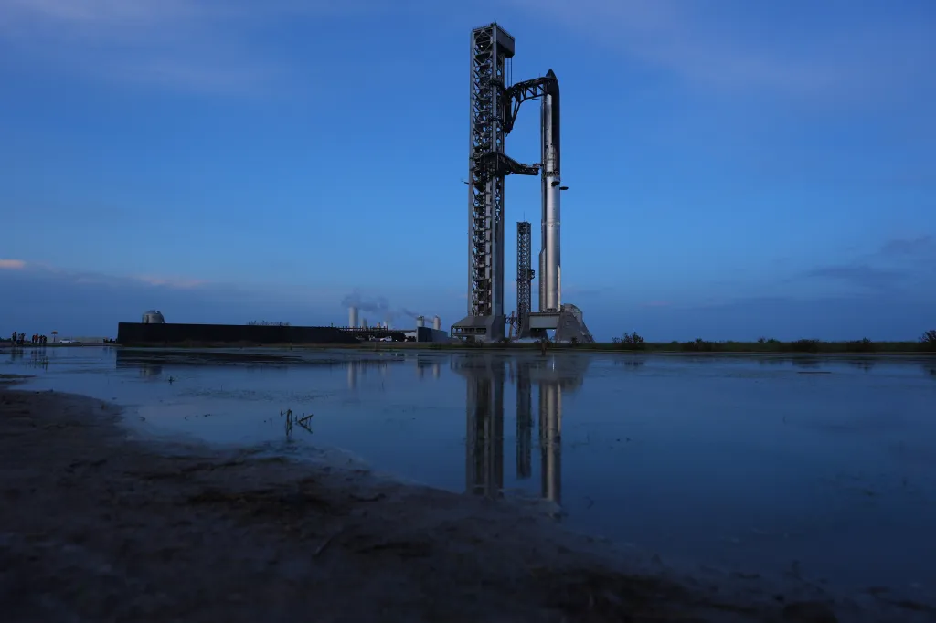 SpaceX Starship sits on the launch pad, reflected in the standing water of a muddy foreground.