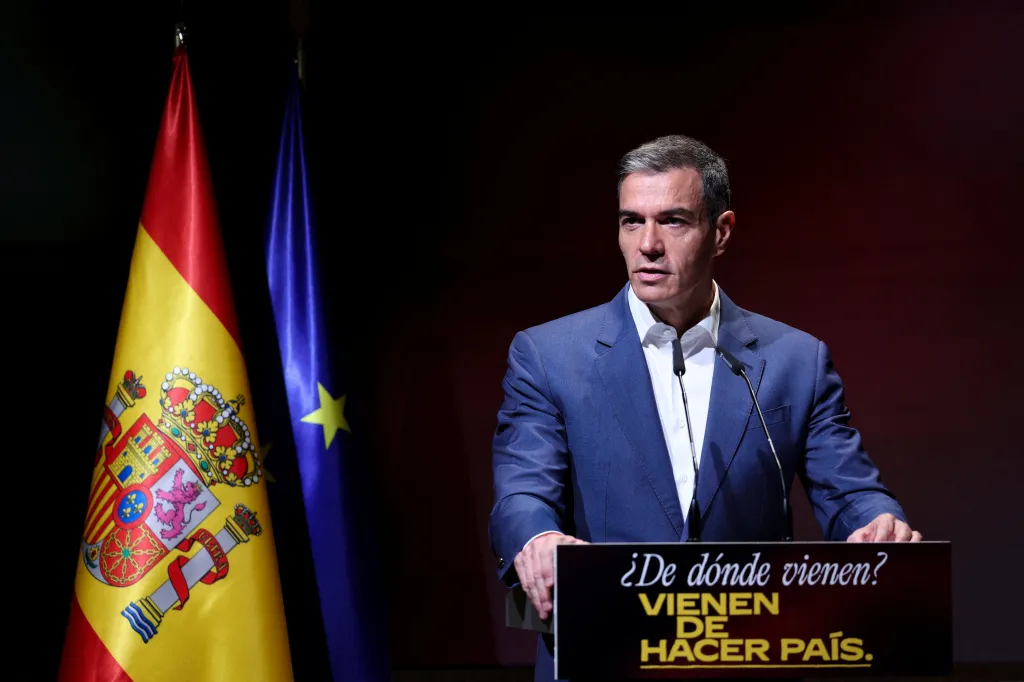 Spanish Prime Minister Pedro Sanchez speaks at a podium with two microphones, with the Spanish and European Union flags behind him.