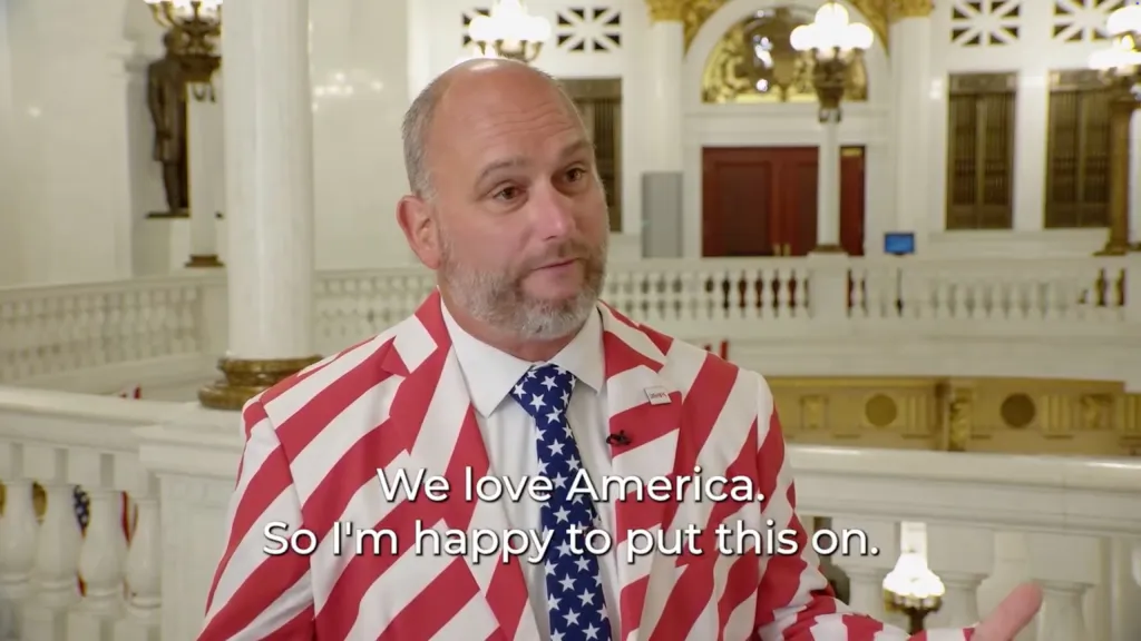 State Rep. Eric Davanzo wearing a red and white striped suit and a blue tie with white stars, with text overlay.