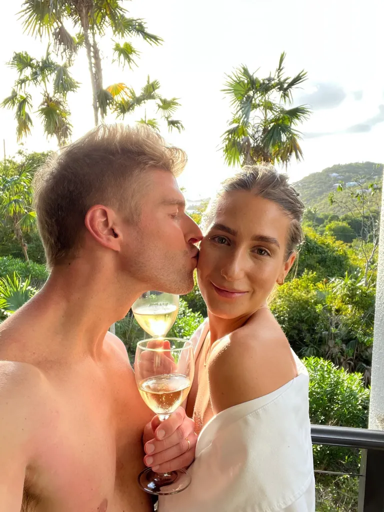 Kyle Cooke kissing Amanda Batula while holding white wine glasses.