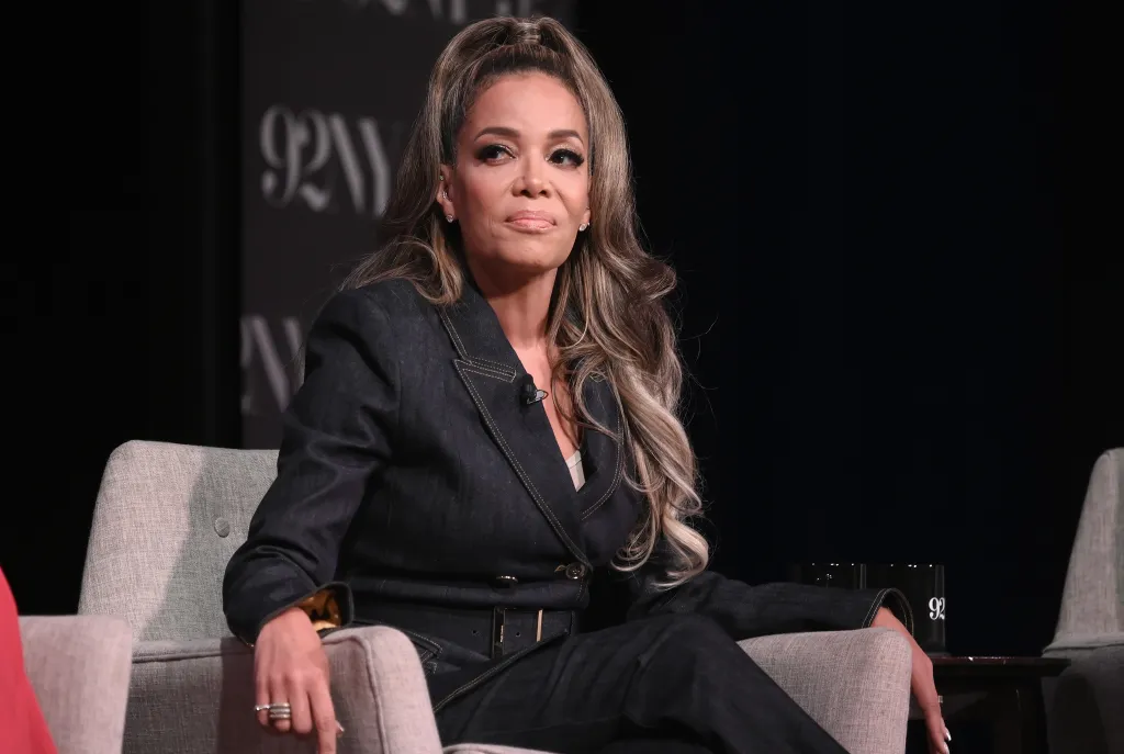 Sunny Hostin sits in a gray armchair wearing a dark denim pantsuit.