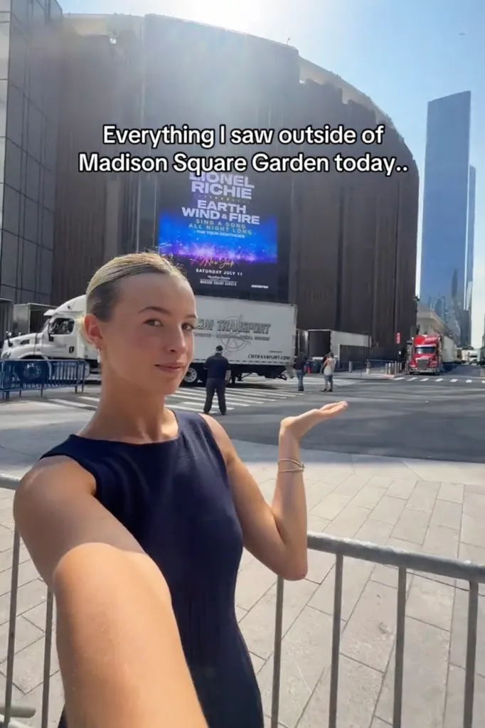 A young woman taking a selfie video in front of Madison Square Garden with a banner advertising Lionel Richie, Earth, Wind & Fire.