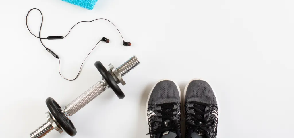 Dumbbell, running shoes, earphones, and a towel on a white background.