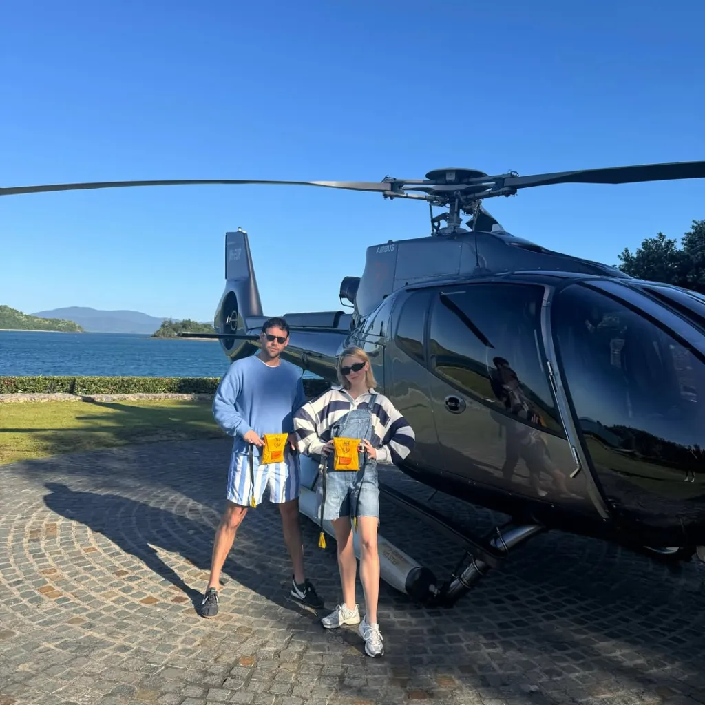 Sydney Sweeney and Scooter Braun standing in front of a helicopter with a body of water in the background.
