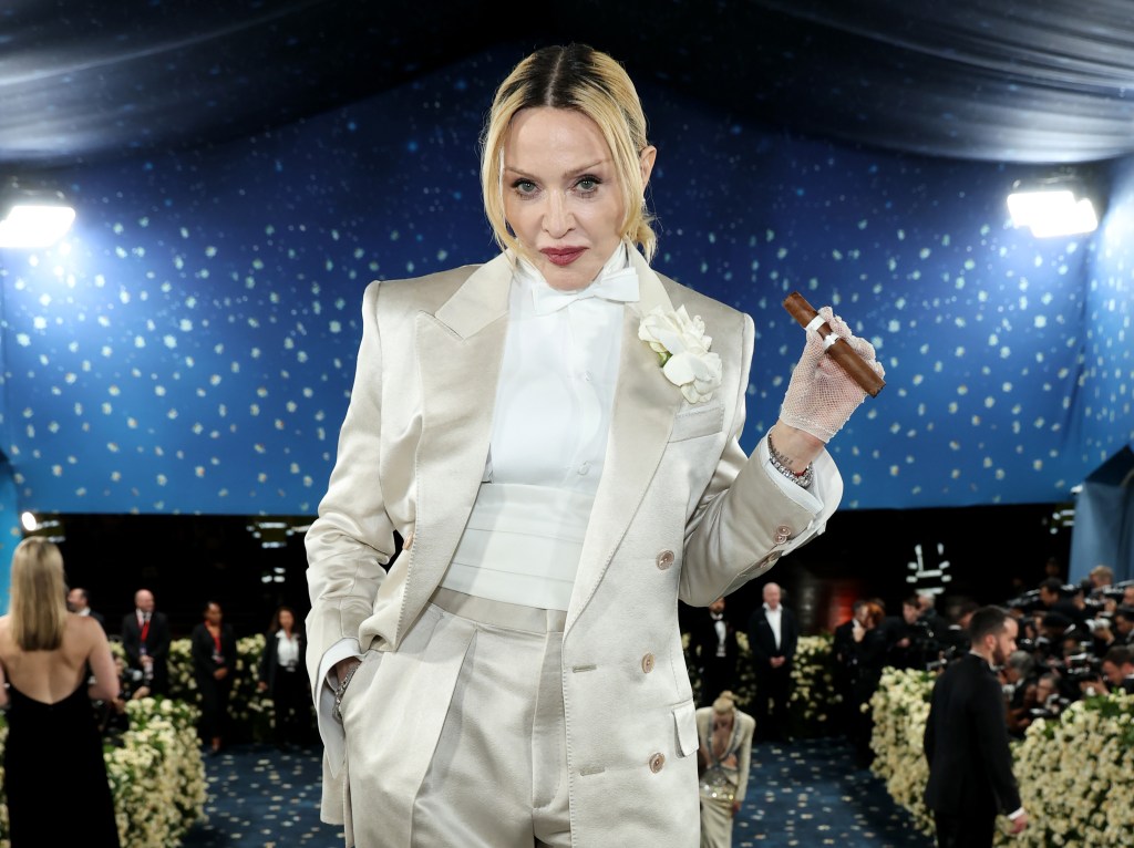 Madonna in an ivory satin suit and white bow tie holds a cigar at the 2025 Met Gala.