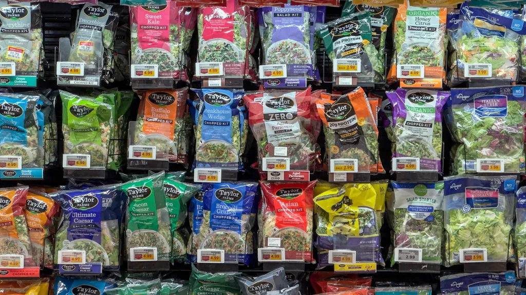 A refrigerated display of various Taylor Farms salad kits, including chopped, power, and salad kits.
