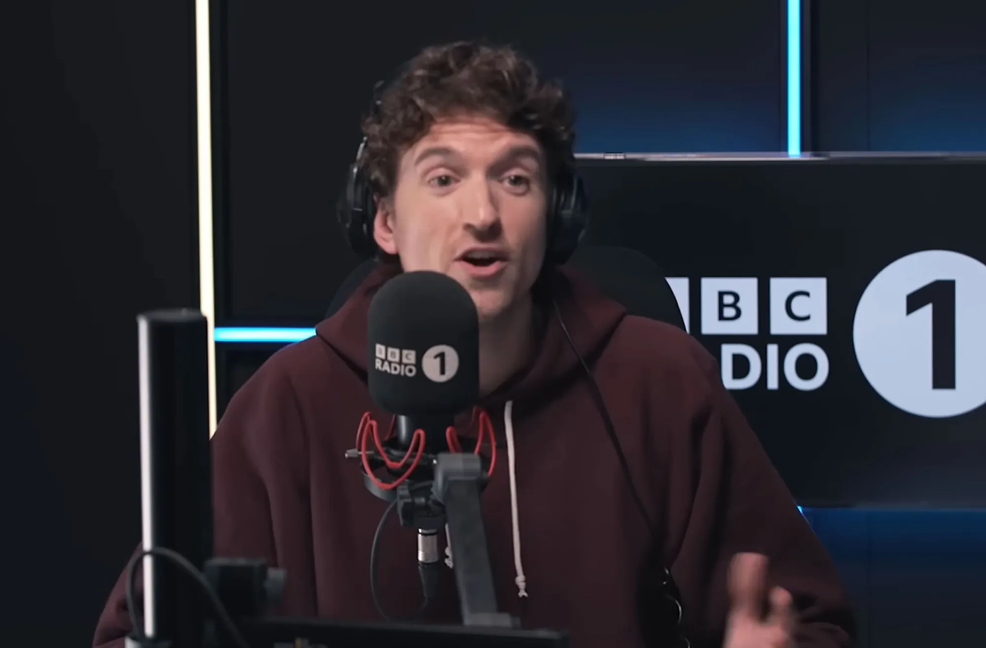 Greg James speaking into a BBC Radio 1 microphone.