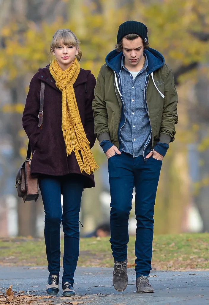 Taylor Swift and Harry Styles walking outdoors in casual winter clothing.
