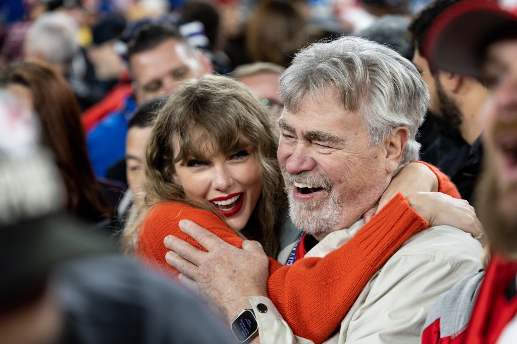 Taylor Swift , in a red sweater, hugging Ed Kielce , in a beige jacket, with a joyful expression.