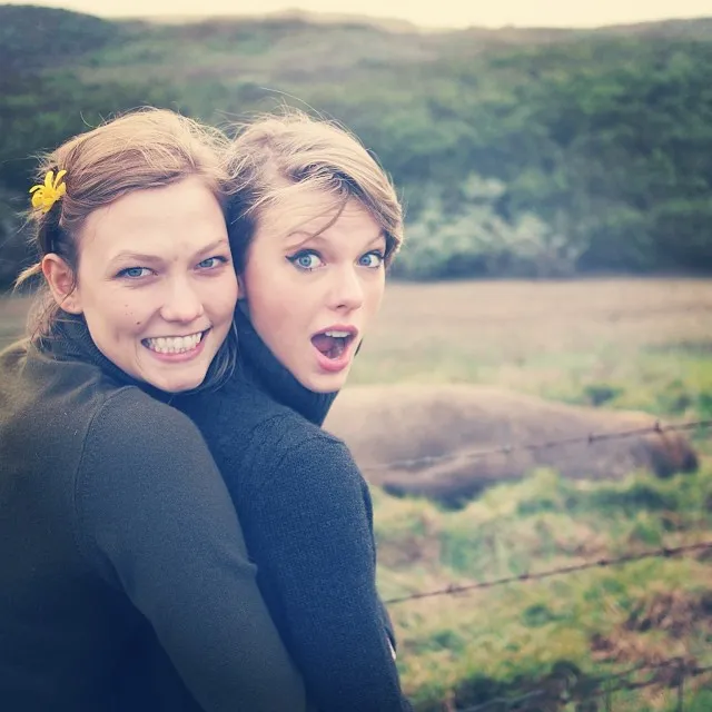 Taylor Swift and Karlie Kloss in a field, Swift with a surprised expression and Kloss with a wide smile.