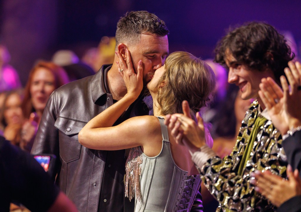 Taylor Swift kissing Travis Kelce while another person applauds at the iHeartRadio Music Awards.