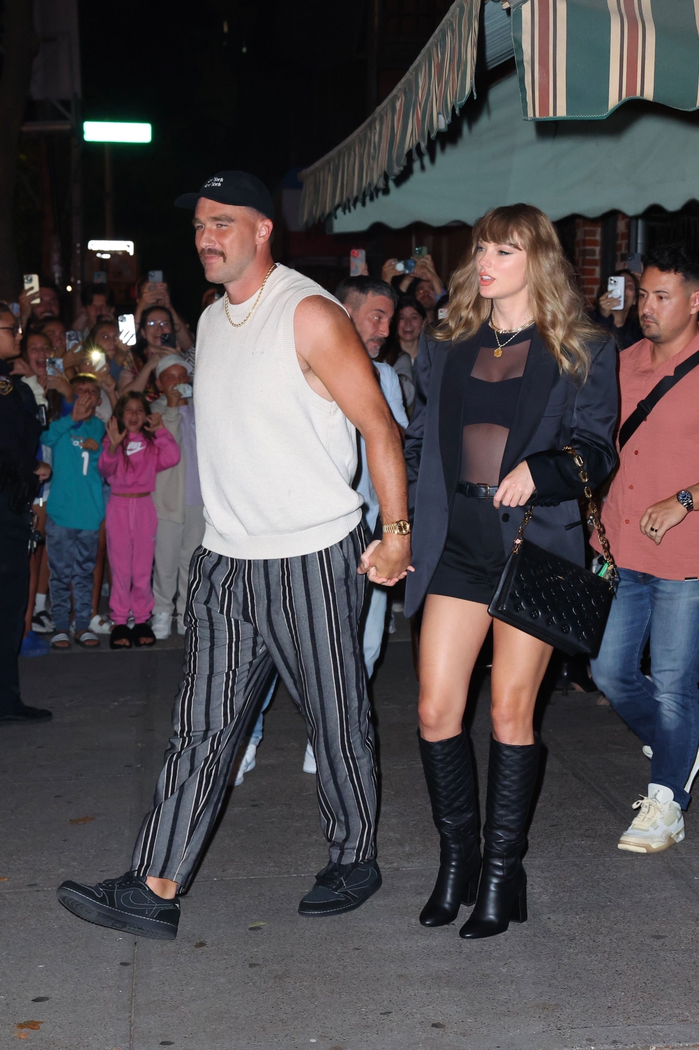 Taylor Swift and Travis Kelce holding hands while leaving Lucali Pizza.