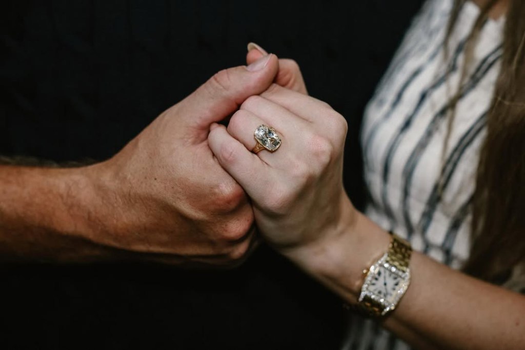 Taylor Swift's engagement ring on her hand as she holds Travis Kelce's hand.