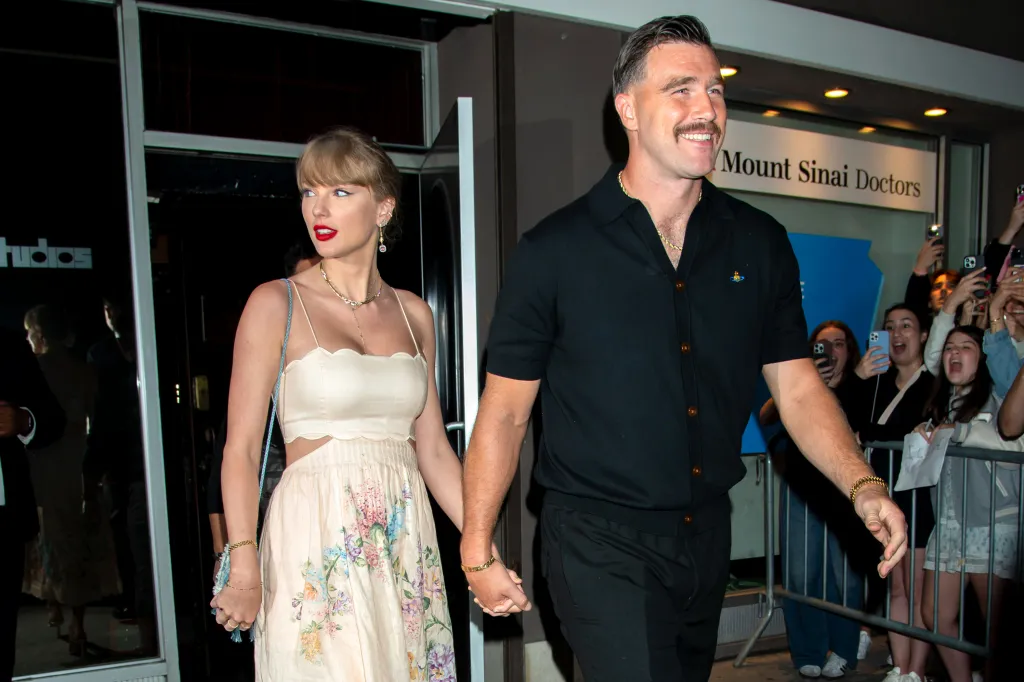 Taylor Swift and Travis Kelce holding hands while leaving an event, with fans taking photos in the background.