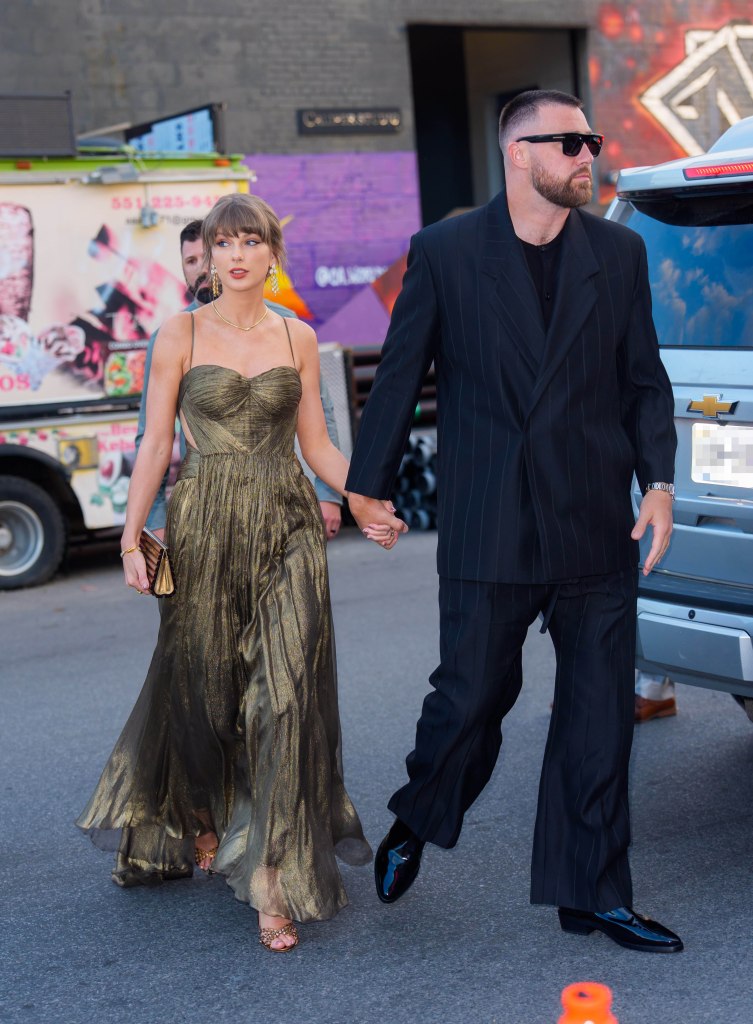 Taylor Swift wearing a gold gown and Travis Kelce wearing a black pinstripe suit walk hand-in-hand in New York City.