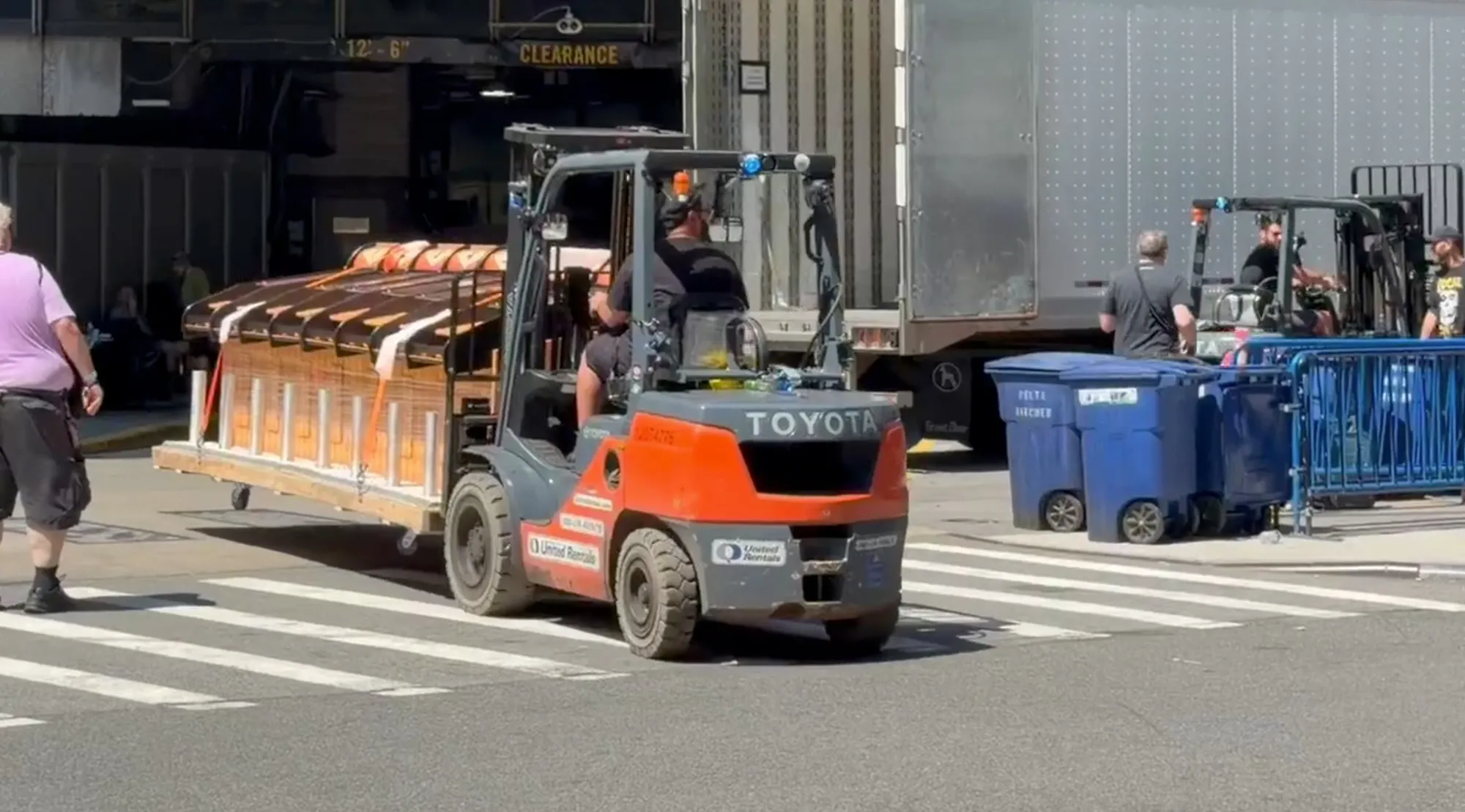 A forklift transporting large, stadium-style seating sections on a wooden pallet.