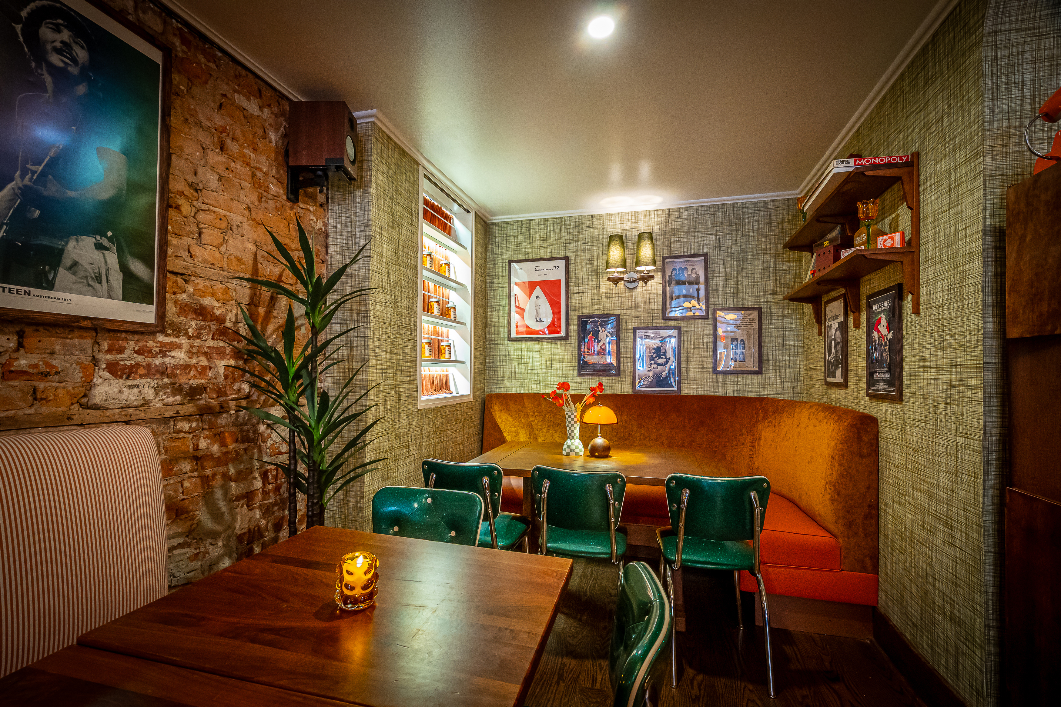 Interior of a restaurant with brick walls, an orange banquette, green chairs, and framed movie posters.