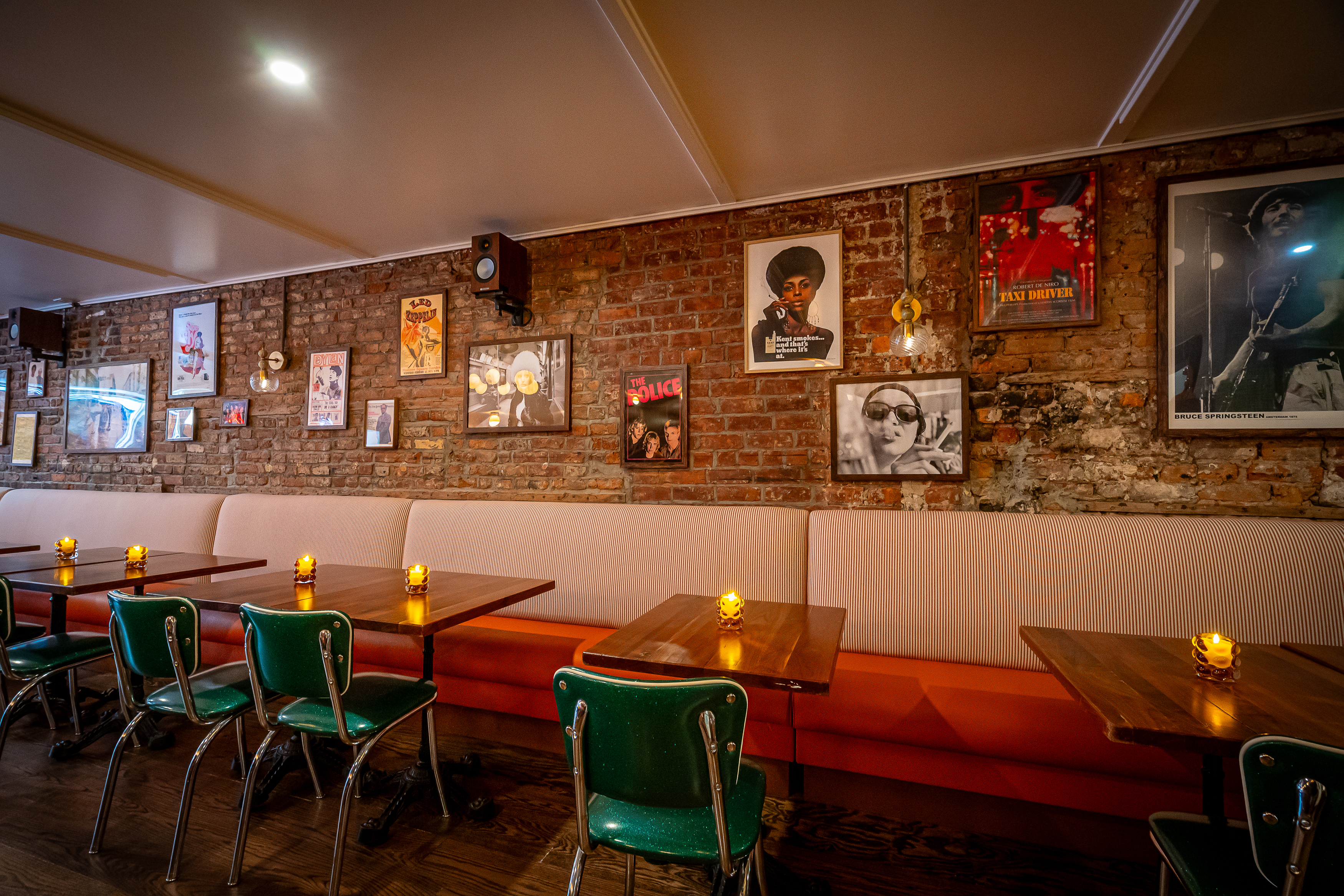Interior of a pizza joint with an exposed brick wall adorned with various posters, including "Led Zeppelin," "The Police," "Taxi Driver," and "Bruce Springsteen Amsterdam 1975."