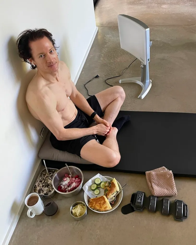 Bryan Johnson sitting next to his health and fitness equipment and meals for Project Blueprint.