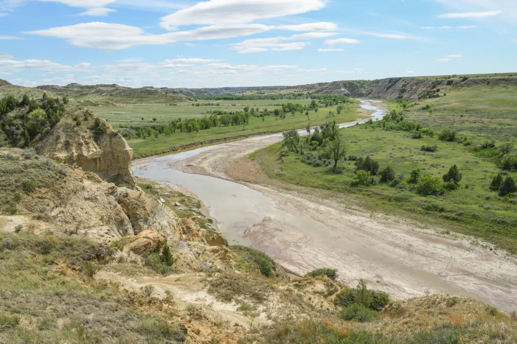 A river winds through a green valley with rocky, arid hills on either side at Teddy Roosevelt National Park.