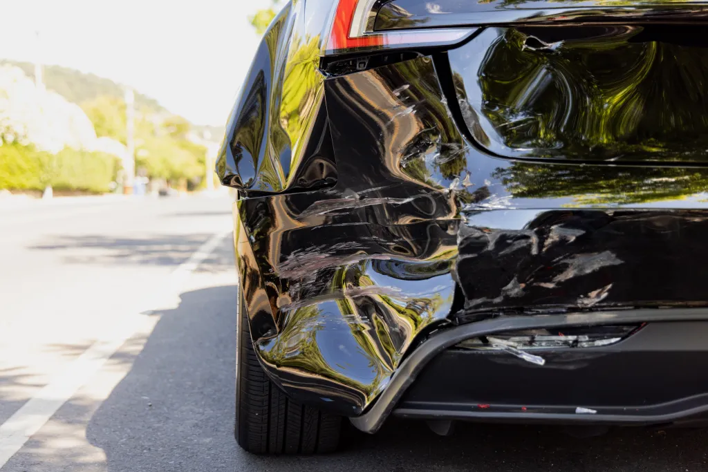 A black Tesla with significant damage to the driver's side rear bumper and quarter panel.