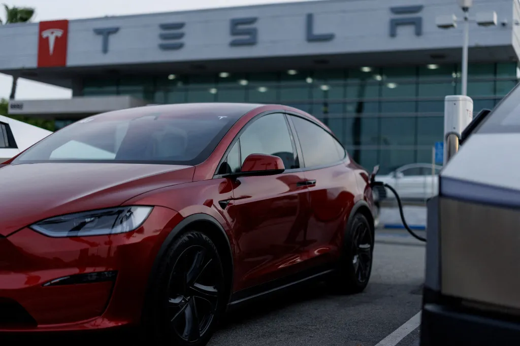 A red Tesla Model Y is charging at a Tesla dealership.