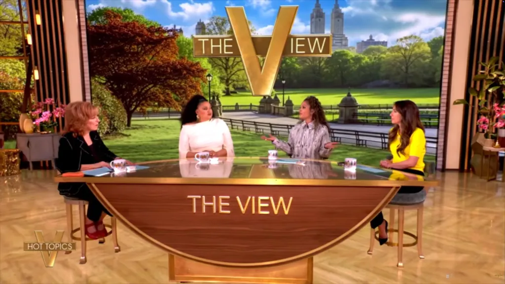 Four women, including Sunny Hostin and Michelle Buteau, sit at "The View" table on a set with a backdrop of a park.