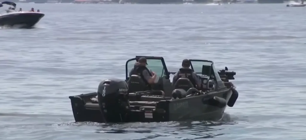 Police patrol boat with two officers on board, on a lake, with another boat in the background.