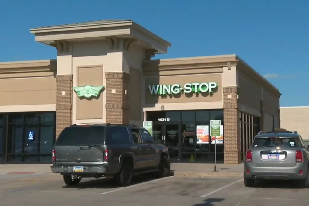 Exterior view of a Wingstop restaurant with parked cars in front.