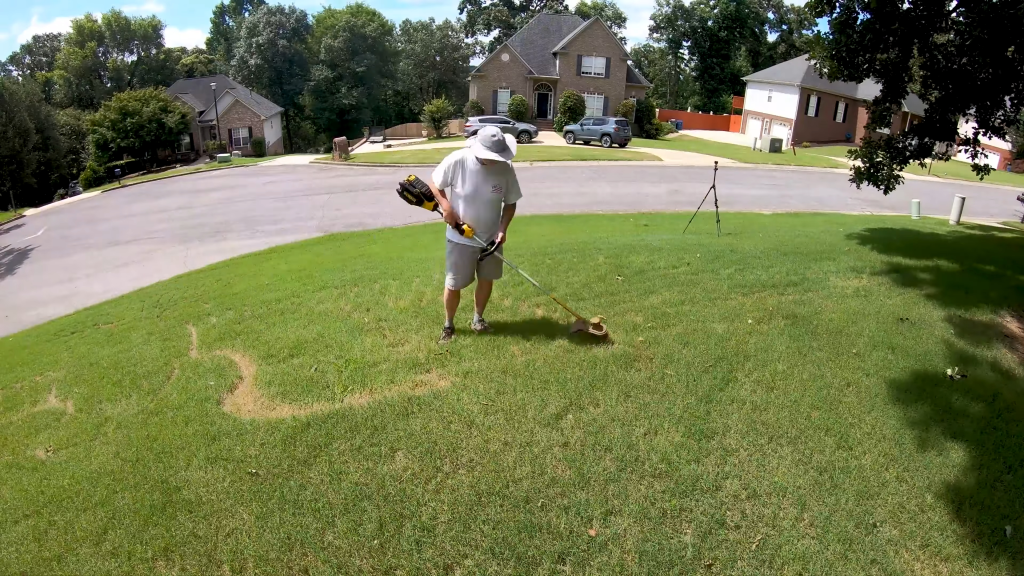Man using a string trimmer to create a grass art piece in his lawn.