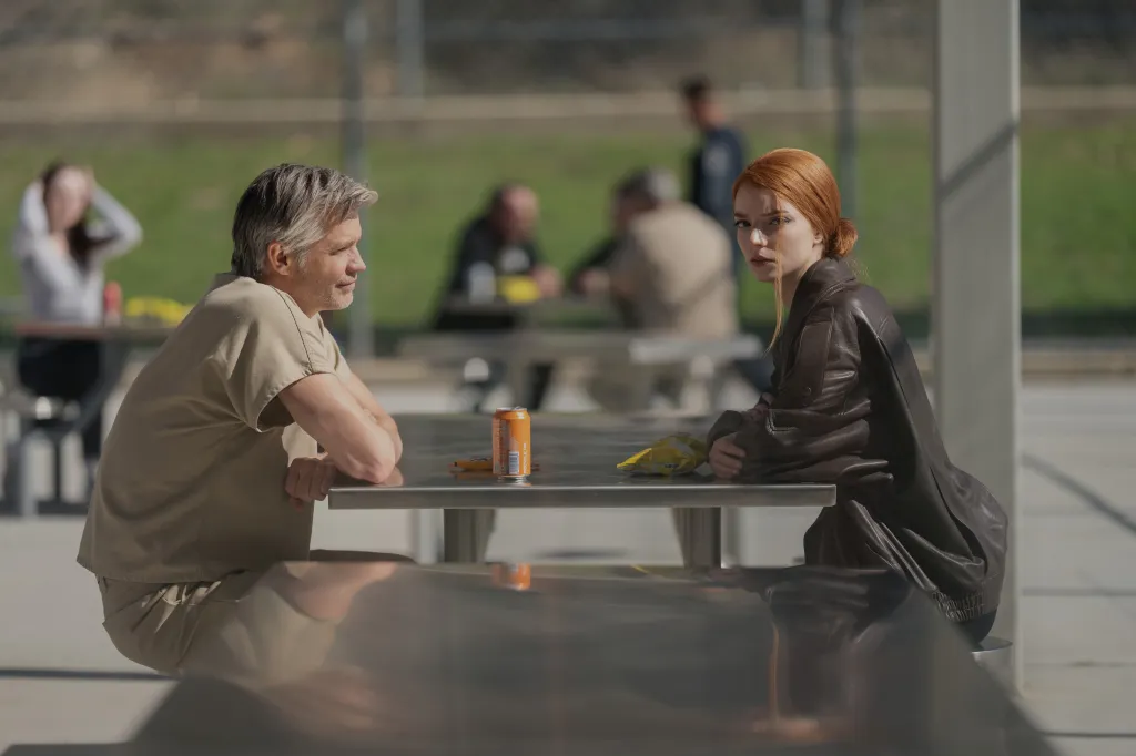 Timothy Olyphant and Anya Taylor-Joy sitting across from each other at a metal table.