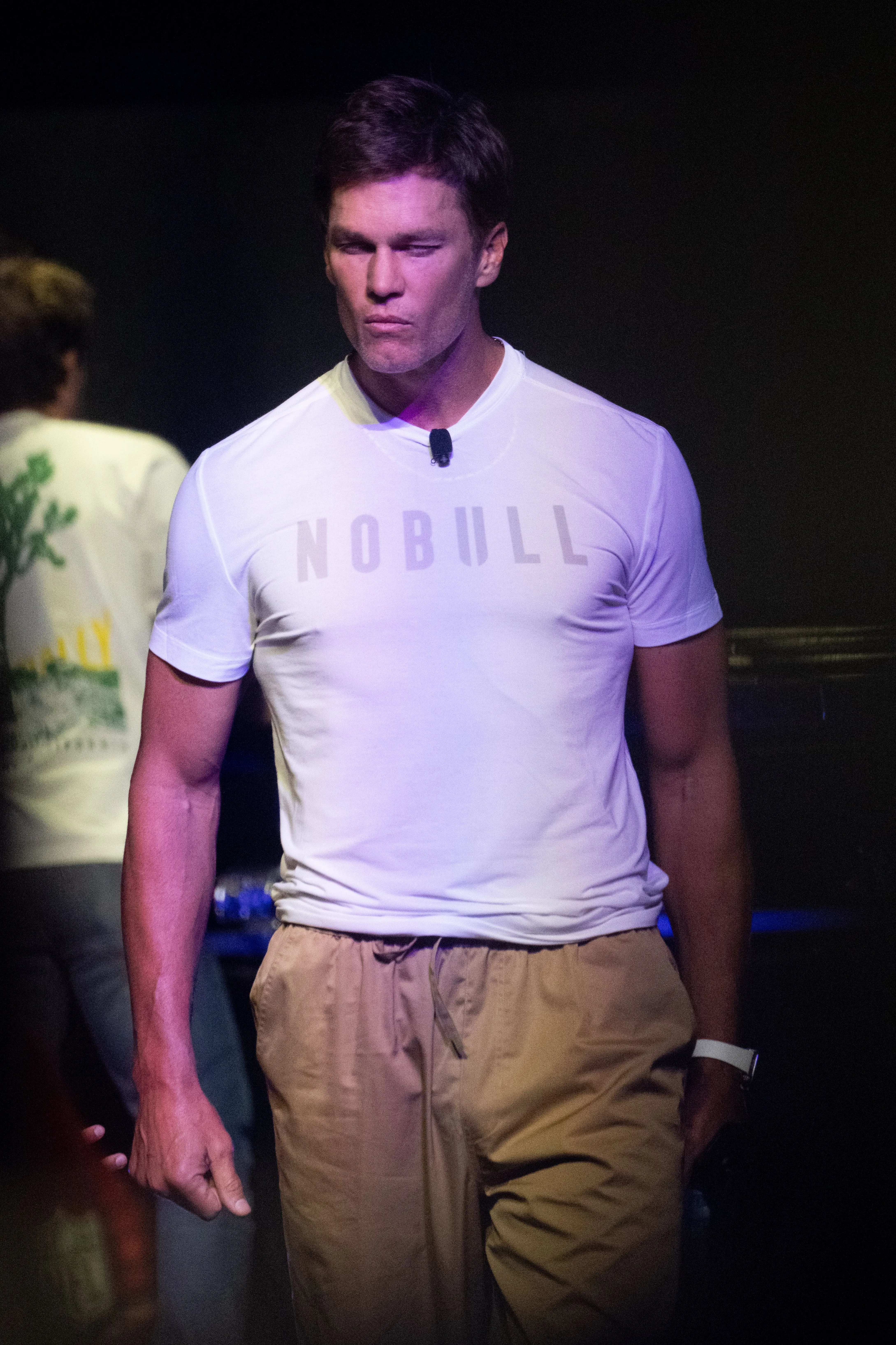 Tom Brady wearing a white "NOBULL" t-shirt and tan pants.