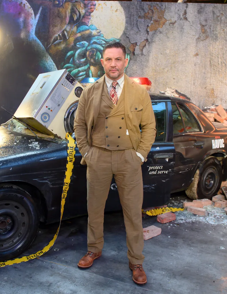 Tom Hardy posing next to a destroyed police car with a washing machine on the hood at The World Premiere of Netflix's Havoc.