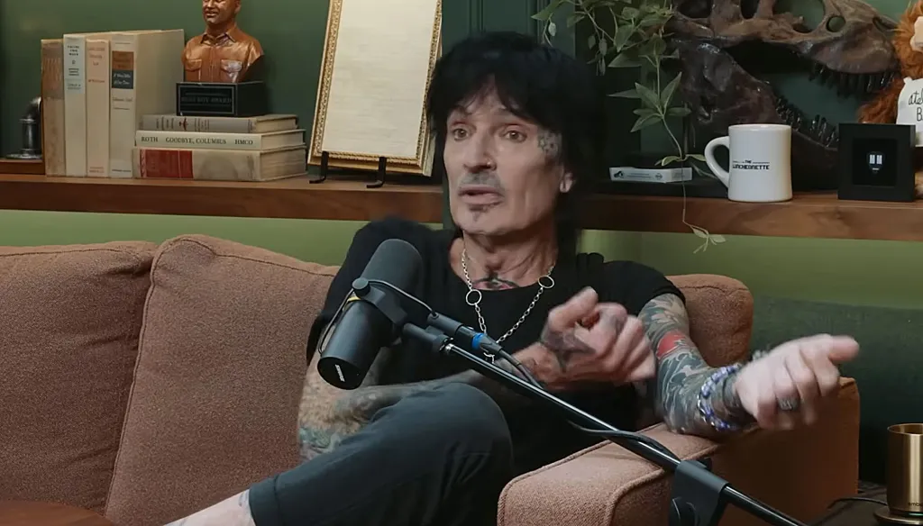 Tommy Lee sitting on a brown couch talking into a microphone.