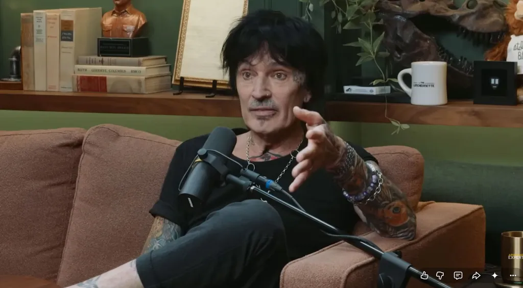 Tommy Lee seated on a couch, speaking into a microphone.