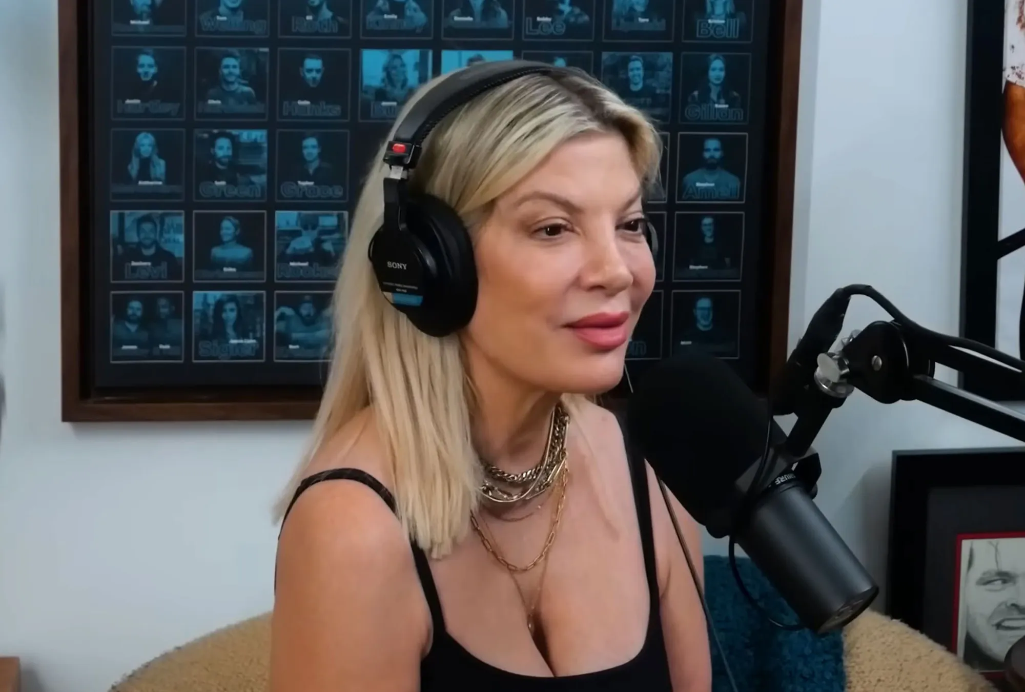 Tori Spelling wearing headphones and a black top, speaking into a microphone.