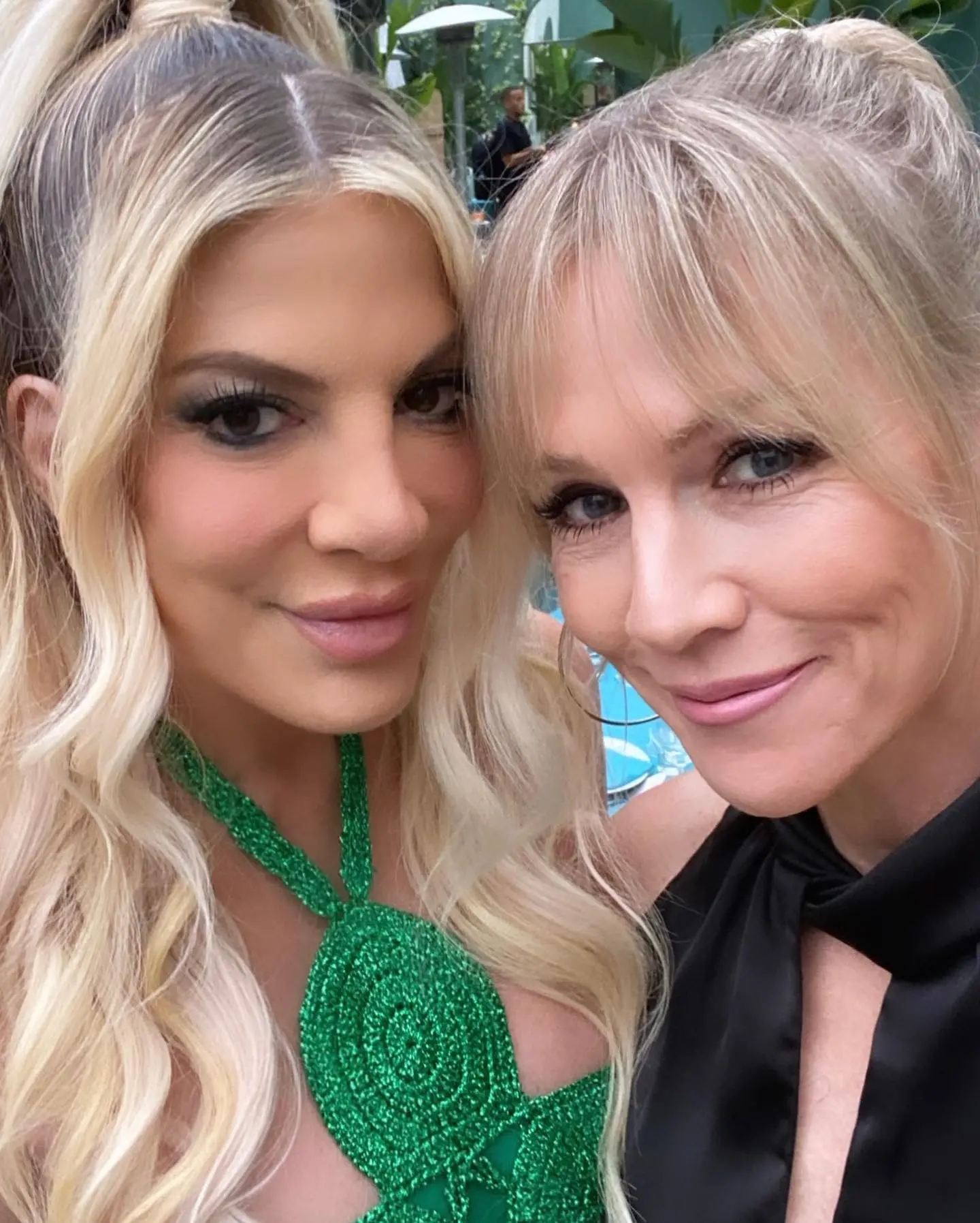Tori Spelling and Jennie Garth pose together, smiling at the camera.