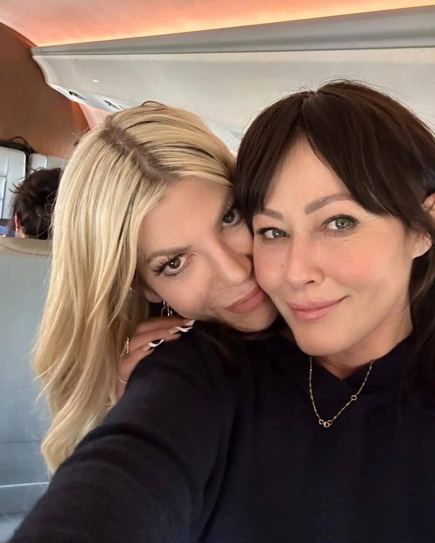 Tori Spelling leaning her face against Shannen Doherty's face.