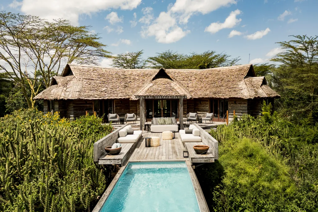 Segera Rhino Roaming Safari lodge with a thatched roof, wooden deck, and a swimming pool surrounded by lush greenery.