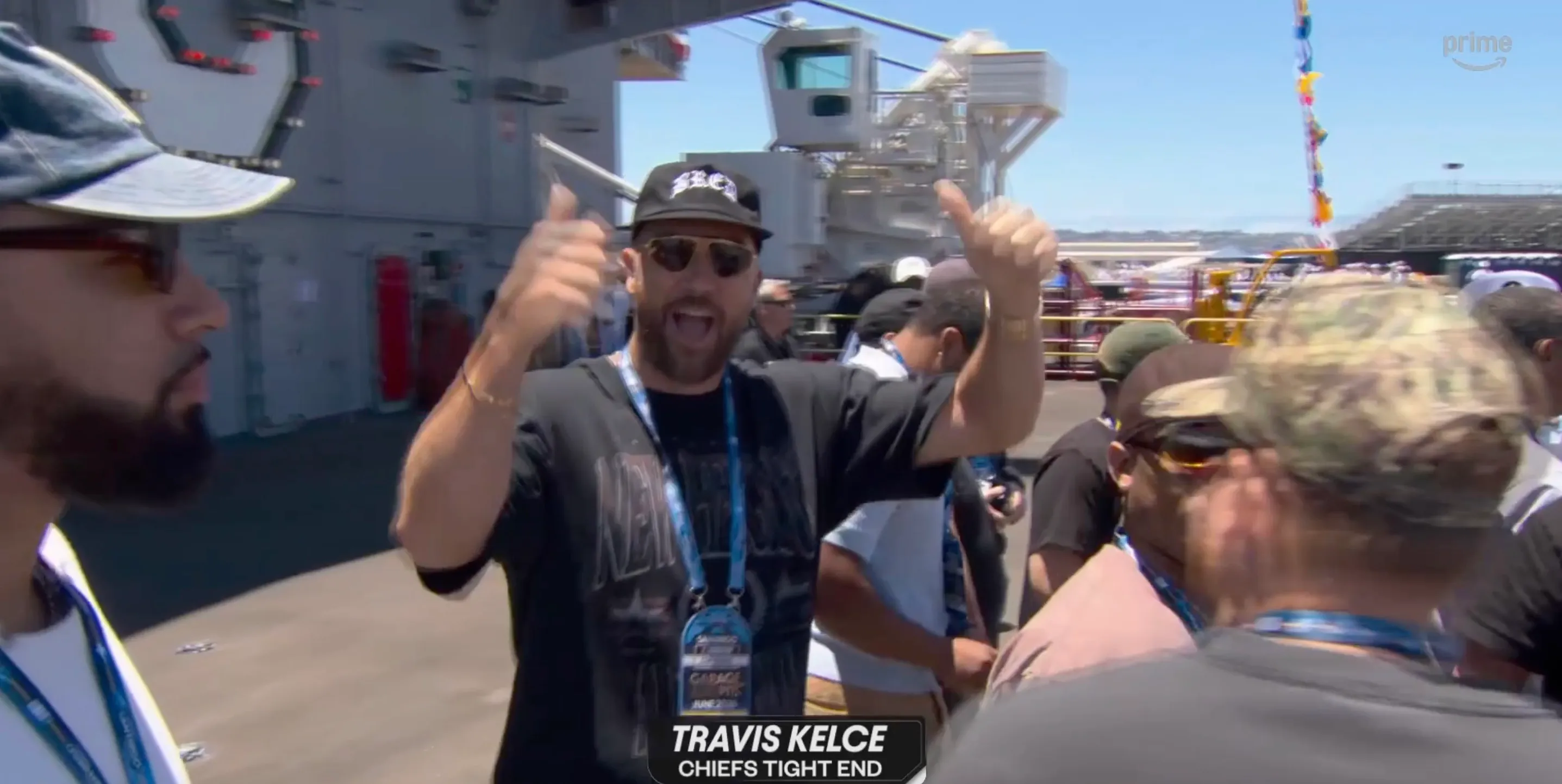 Travis Kelce giving thumbs up at a NASCAR event.